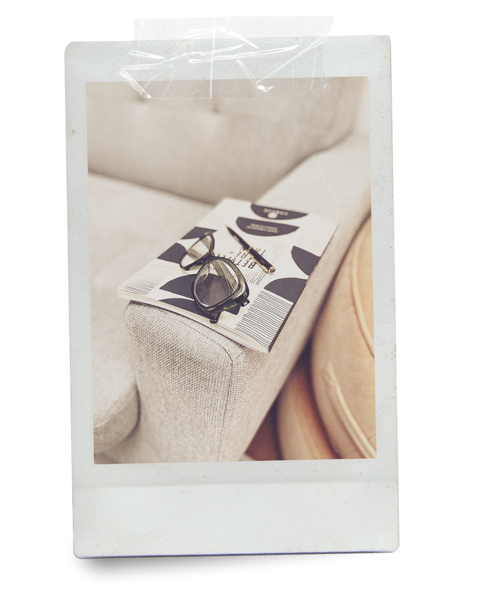 Journal on a gray couch with reading glasses and a pen
